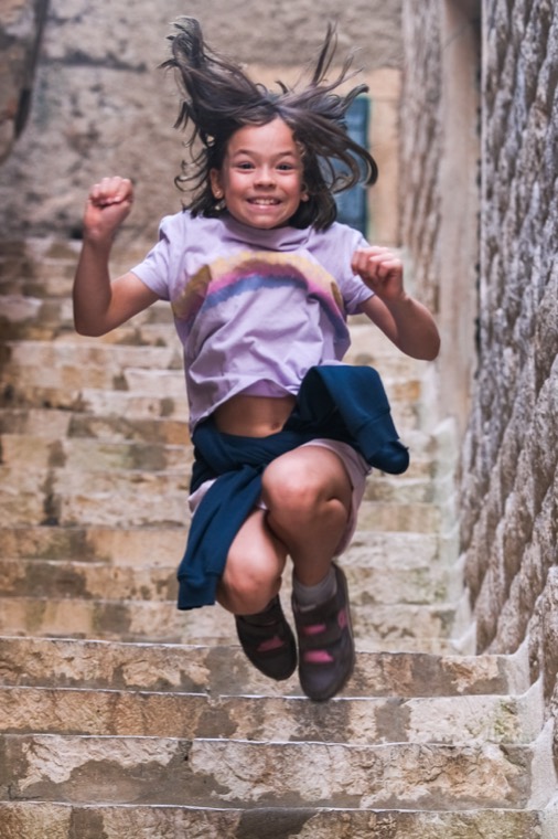 A girl leaping down ancient stone steps, hair flying, Dubrovnik